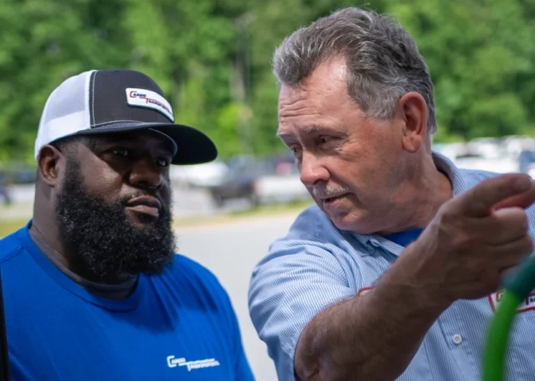 Two men engaged in a discussion at a freight trucking company, one pointing at equipment.