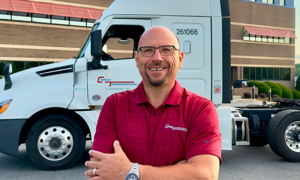 A CDL A Driver in a red shirt smiling in front of a Cargo Transporters truck in Claremont, NC.