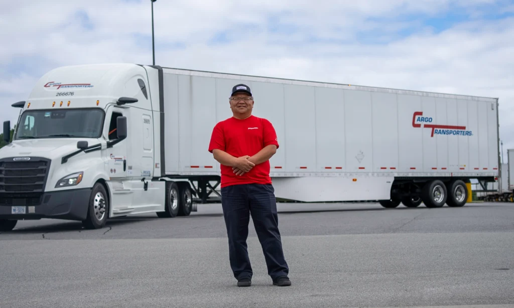 A dedicated trucking company driver stands in front of a Cargo Transporters truck in the Charlotte NC region, showcasing pride in his work.