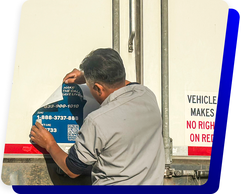 An employee applies an anti-trafficking awareness decal to a trucking and logistics trailer near Charlotte, promoting safety and advocacy.