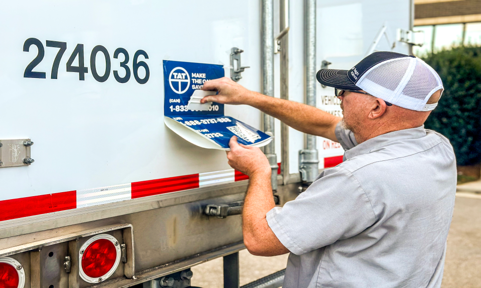 A trucking and logistics company employee applies a safety awareness decal near Charlotte to enhance driver and public safety.